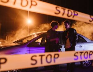 police officer speaking to a man, standing by a car at night behind crime scene tape
