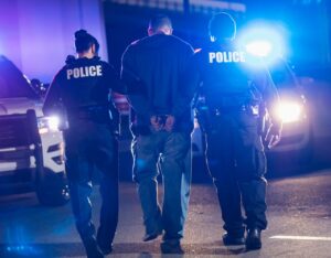 tall man arrested with hands handcuffed behind back in between two cops